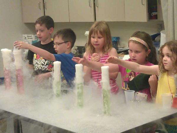 five children perform a bubbling science experiment in large test tubes